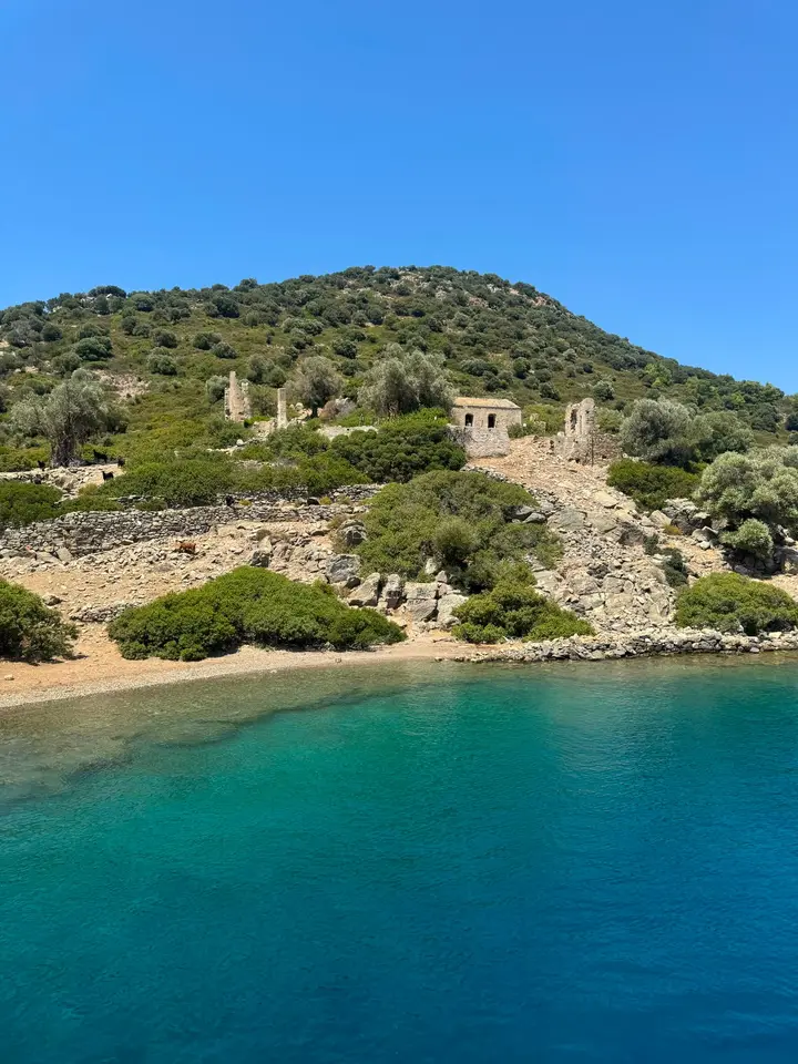 Turquoise bay below a green hill with old stone ruins
