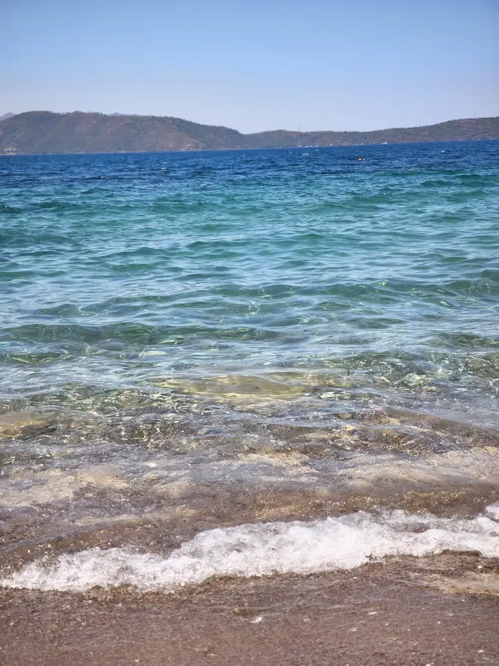 Small waves on a pebble beach, with hills across the bay
