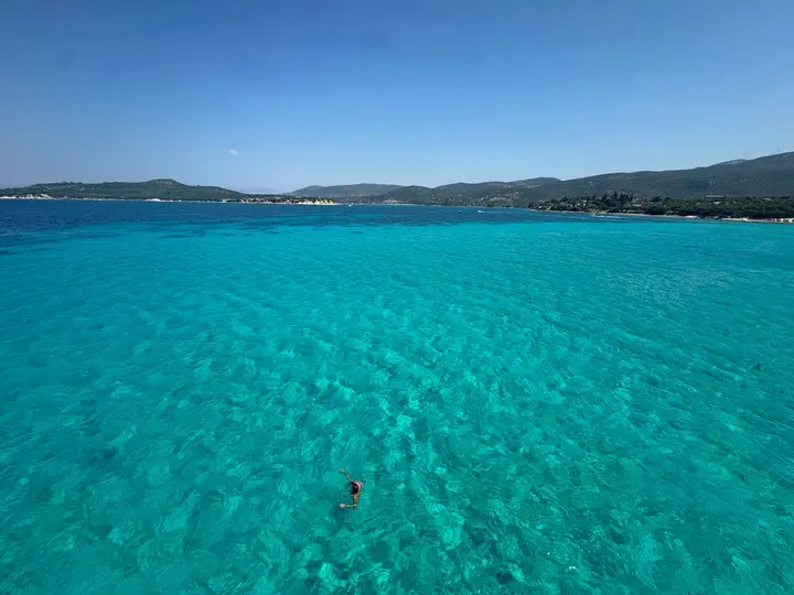 Clear turquoise water of a wide bay with green hills on the horizon