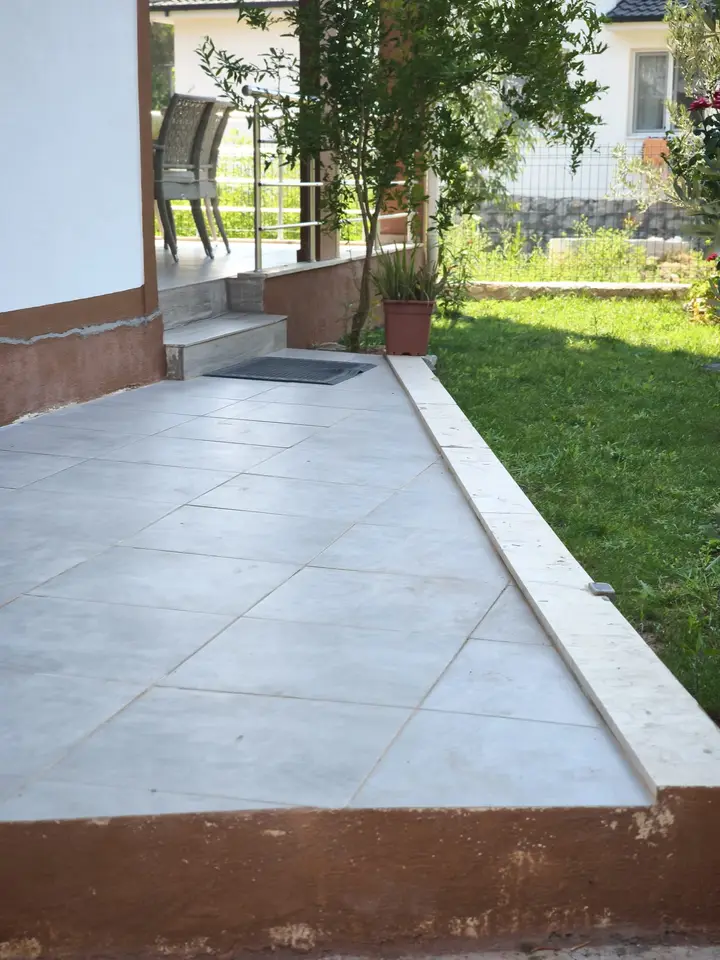 Tiled patio next to the lawn, with steps up to the terrace